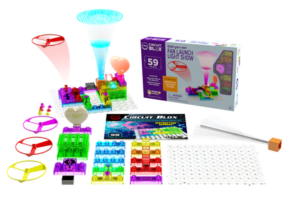 The Circuit Blox™ 59 project Student Set by E-Blox®, an educational electronic kit with 59 pieces, features components such as fans, lights, connectors, and a grid. The kit box displays a completed setup alongside various spread out parts including propellers, a manual aligned with NGSS requirements, and a fiber optic component.