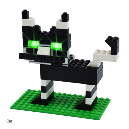 A small, black and white block toy cat with green, illuminated eyes stands on a green rectangular base. The toy cat has a raised blocky tail and pointy ears. Perfect for introducing STEM concepts, the word "Cat" is written in the bottom left corner of the image. This delightful creation is part of the Power Blox™ Builder 292 Classroom Set by E-Blox®, featuring their LED Light-Up Building Blocks.