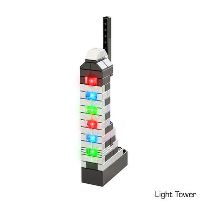 The Power Blox™ Builds Plus Set - E-Blox® from E-Blox features an LED light-up tower model with multiple rectangular colored lights, including red, blue, and green, on its sides. The base is black, constructed using Power Blox bricks, while the rest of the structure incorporates white, black, and gray pieces. "Light Tower" is labeled at the bottom right corner and aligns with STEM curriculum concepts.