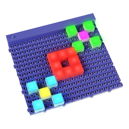 The Lite Blox Classroom Set by E-Blox features a blue pegboard equipped with LED Blox that hold various illuminated squares in colors like red, green, pink, yellow, and blue. The squares create distinct patterns with a prominent red square in the center and other colored squares scattered around to stimulate creativity.