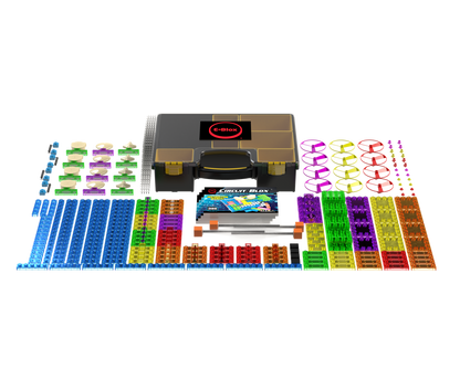 The Circuit Blox™ 395 Project Classroom Set from E-Blox features a neatly arranged collection of brightly colored building components, including blue, green, red, purple, and orange pieces. These elements are distributed around a central box labeled "Circuit Blox." The set includes blocks, connectors, and other electronic components that adhere to NGSS requirements.