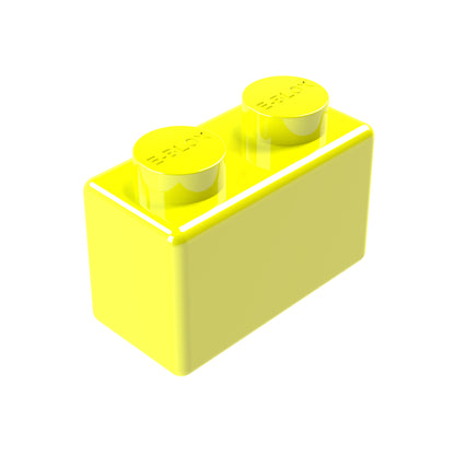 A bright yellow E-Blox 1x2 plastic building block with two round studs on top stands out against a plain white background. It is available in seven vibrant colors.