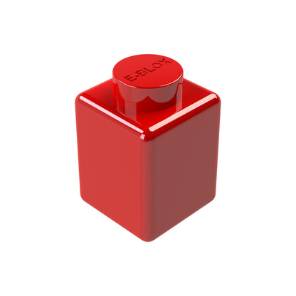 A single red E-Blox 1x1 Block with a round knob on top rests on a white background. "E-BLOX" is embossed on the knob. This piece is part of a 7-color set and includes conductive tin for enhanced connectivity.