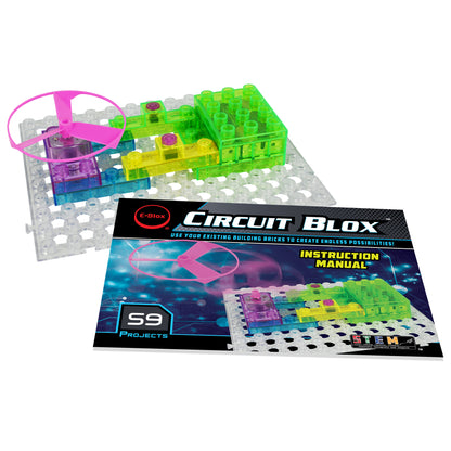 A colorful STEM toy set called "Circuit Blox™ 59 - E-Blox® Circuit Board Building Blocks Toys" by E-Blox is displayed. The toy consists of translucent building blocks in various colors, assembled on a clear base grid. A pink propeller is attached to the blocks, demonstrating electricity in action. An instruction manual showing 59 building projects is also visible.