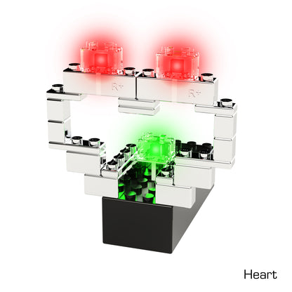 A Power Blox™ heart crafted from black and white bricks, featuring two red LED blocks at the top and a green LED block at the center. The structure is mounted on a black base, showcasing E-Blox's patented technology. The word "Heart" is written in the bottom right corner.