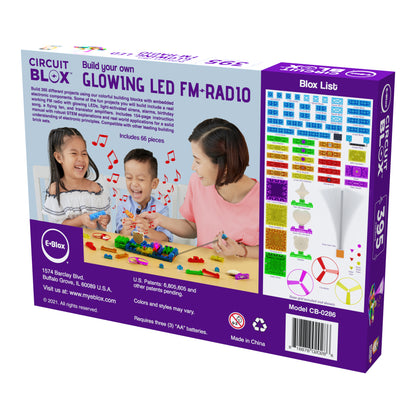 The image shows the back of a Circuit Blox™ 395 - E-Blox® Circuit Board Building Blocks toy box. It depicts a family engaged in a STEM program, playing with colorful circuit blocks. The box includes 66 pieces that can be used to build various working circuits, such as a glowing LED FM radio. A list of components and contact information is visible.