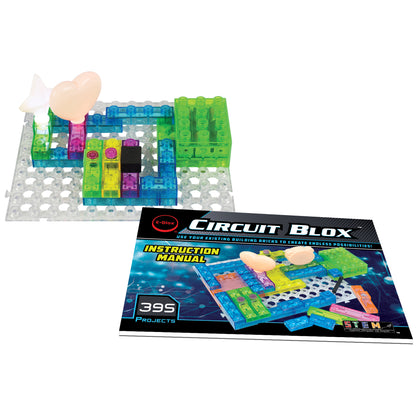 A STEM educational kit called Circuit Blox™ 395 - E-Blox® Circuit Board Building Blocks Toys for Kids from E-Blox is shown. The set features transparent colored building bricks on a perforated base and includes electronic components like a light bulb and an FM radio. Positioned in front of the project is an instruction manual labeled "395 Building Projects," making it perfect for any STEM program.