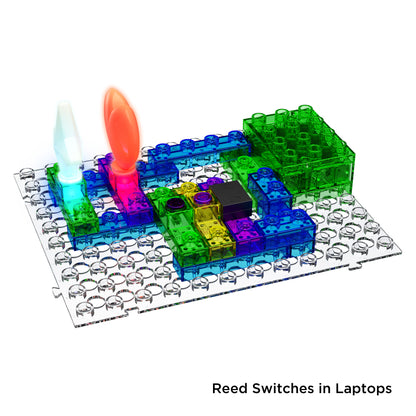 The Circuit Blox™ 395 Project Student Set from E-Blox® is a vibrant electronic building kit that includes interlocking clear plastic pieces arranged on a grid board. The set features two light-up components, one emitting white light and the other red. Additionally, text in the bottom right corner reads "Reed Switches in Laptops," meeting NGSS standards.