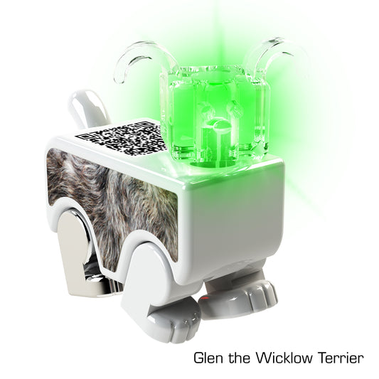 The LUMEN®- Glen- Illuminated Mini Figure by E-Blox, Inc. features a digital toy dog with a rectangular body, a furry texture on its side, and a QR code on its back. Its head is a transparent green block that emits light. Dubbed "Glen the Wicklow Terrier," this enchanting mini figure brings imagination to life.