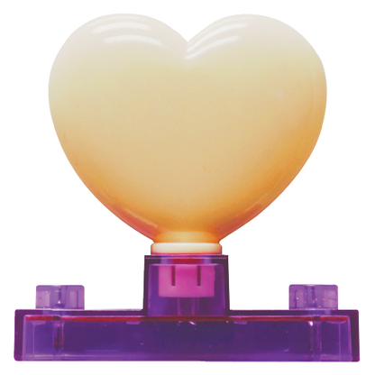 The Circuit Blox™ - LED Heart Block by E-Blox® features a heart-shaped LED block with a gradient color transitioning from cream to orange at the top. It is mounted on a transparent purple stand supported by two small rectangular legs. This decorative item or night light is perfect for adding a cozy glow to any room.