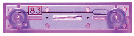 Close-up view of a purple audio cassette tape with the number "83" in red text on a white background displayed in the top left corner. The transparent tape reveals inner mechanisms, reminiscent of the intricate design found in E-Blox's Reed Switch Block for Circuit Builder.